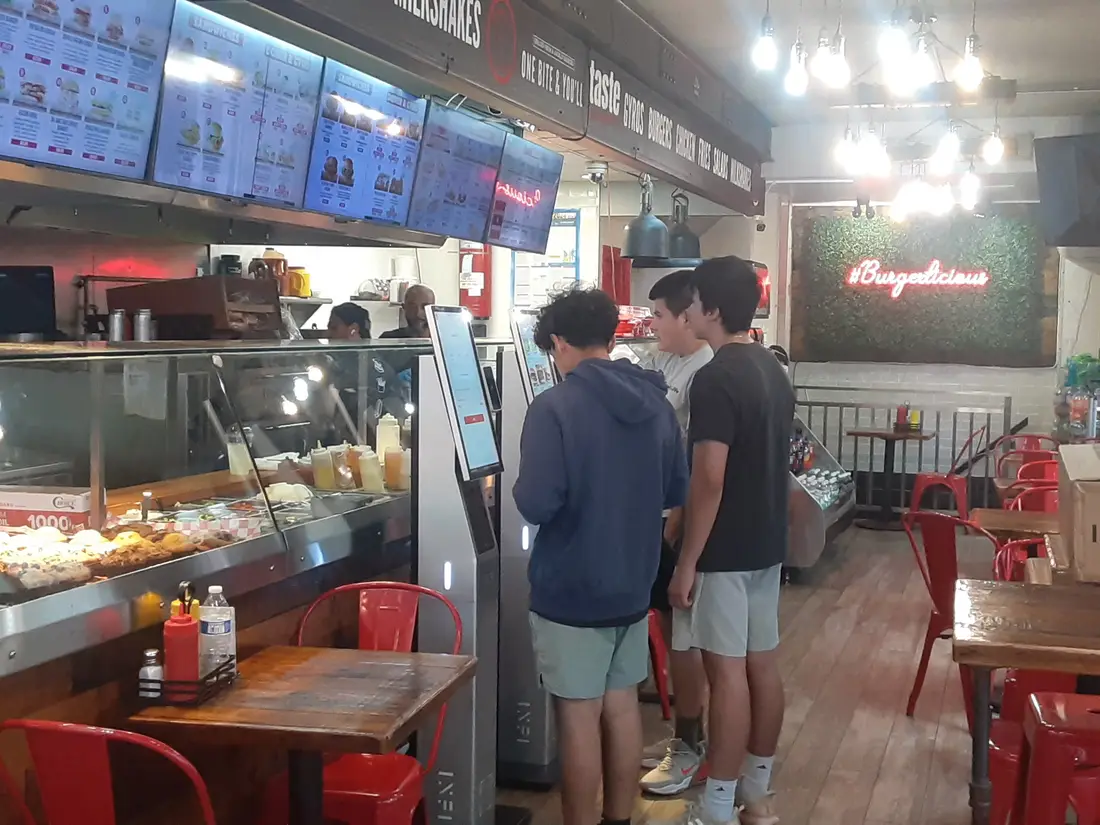 Friends ordering at INFI kiosks in a burger shop